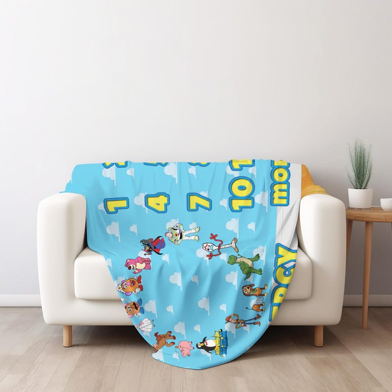 May include: A light blue fleece blanket featuring a repeating white cloud pattern and various Toy Story character illustrations. The blanket displays yellow numbers and the text 10 11 12 months, along with a vertical yellow Toy Story logo on the side.