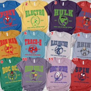 May include: A collection of twelve colorful t-shirts featuring various superhero characters. Each shirt displays a character's name in bold letters, accompanied by a graphic and the text "Spidey and His Amazing Friends". The shirts are in various colors, including blue, yellow, and red.
