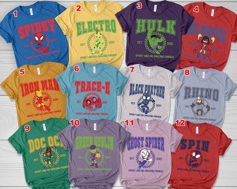 May include: A collection of twelve colorful t-shirts featuring various superhero characters. Each shirt displays a character's name in bold letters, accompanied by a graphic and the text "Spidey and His Amazing Friends". The shirts are in various colors, including blue, yellow, and red.