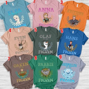 Puede incluir: Una colecci&oacute;n de nueve camisetas de manga corta en varios colores, cada una con un personaje de la pel&iacute;cula "Frozen". Las camisetas muestran nombres de personajes como Elsa, Anna, Kristoff y Olaf, junto con la palabra "Frozen".