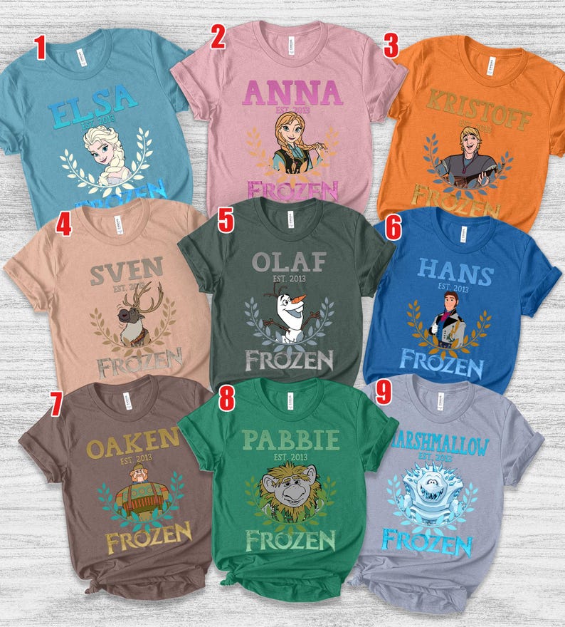 Puede incluir: Una colecci&oacute;n de nueve camisetas de manga corta en varios colores, cada una con un personaje de la pel&iacute;cula "Frozen". Las camisetas muestran nombres de personajes como Elsa, Anna, Kristoff y Olaf, junto con la palabra "Frozen".