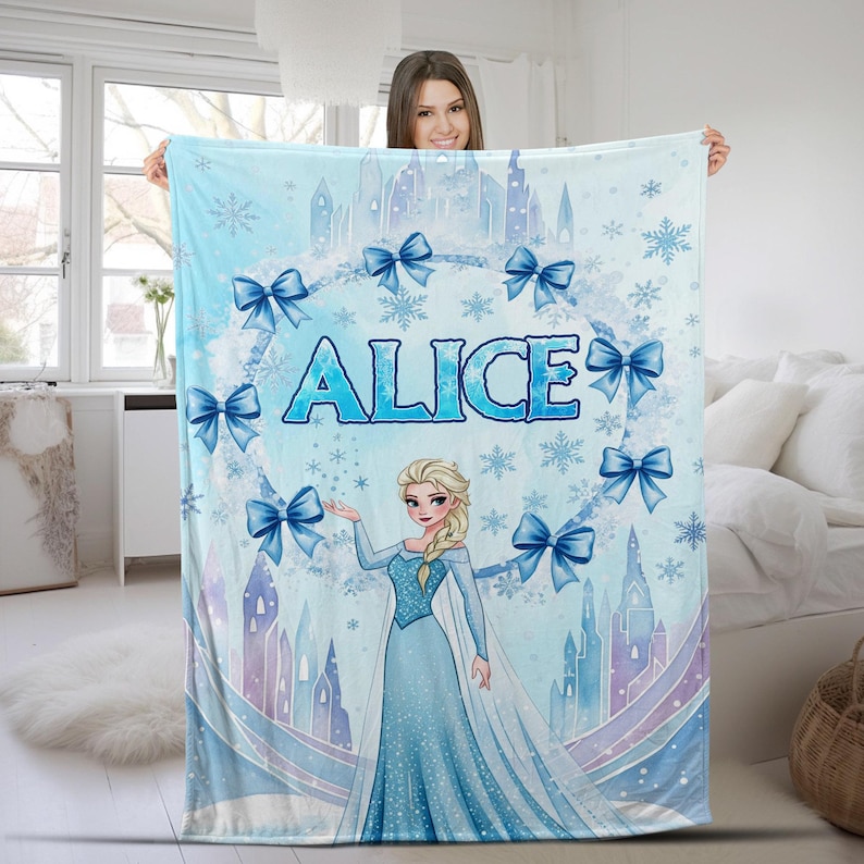 May include: A light blue fleece blanket featuring a printed illustration of a blonde character in a long blue gown, a castle silhouette, snowflakes, and blue bows. The name ALICE is printed in large blue letters in the center of the design.