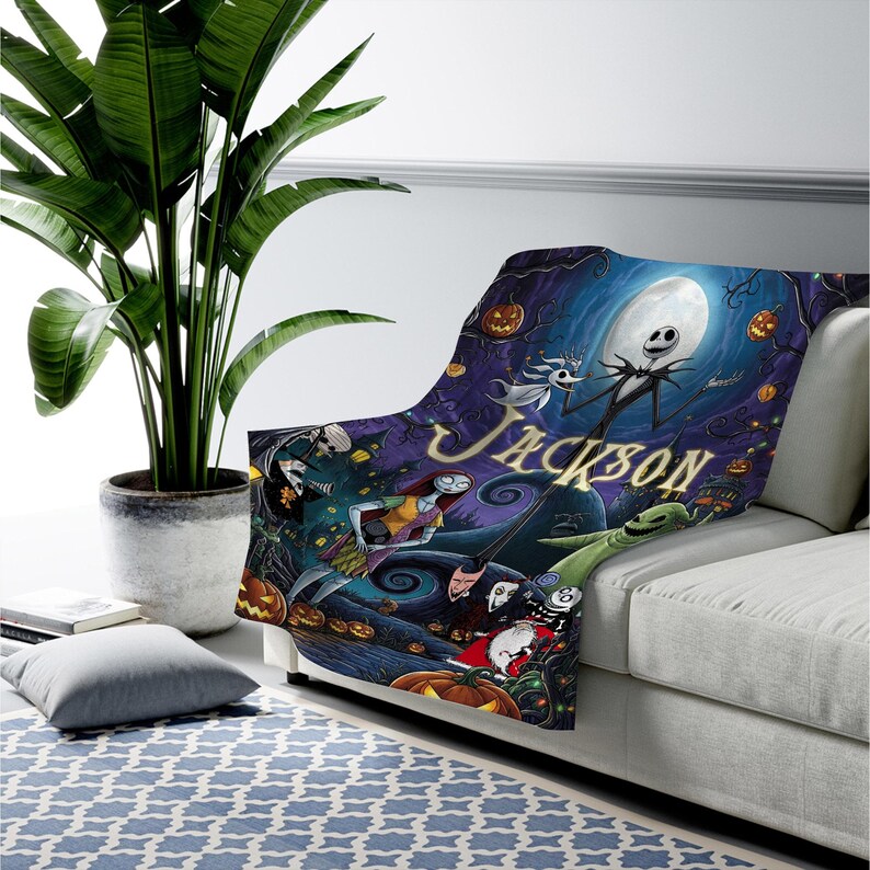 K&ouml;nnte beinhalten: Eine Pl&uuml;schdecke mit einer dunklen, fantastischen Szene aus Nightmare Before Christmas mit Charakteren wie Jack Skellington, Sally und Zero. Das Design zeigt einen gro&szlig;en Vollmond, orangefarbene K&uuml;rbisse und den Namen Jackson in Gold.