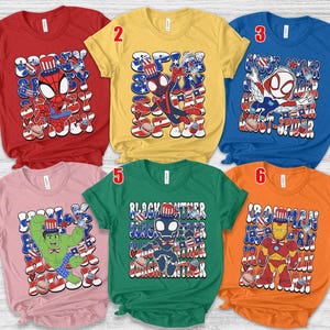 K&ouml;nnte beinhalten: Sechs kurz&auml;rmelige T-Shirts in verschiedenen Farben, jedes mit einem Superhelden-Motiv mit patriotischen Themen. Die Shirts zeigen Charaktere wie Spider-Man, Ghost-Spider, Hulk, Black Panther und Iron Man.