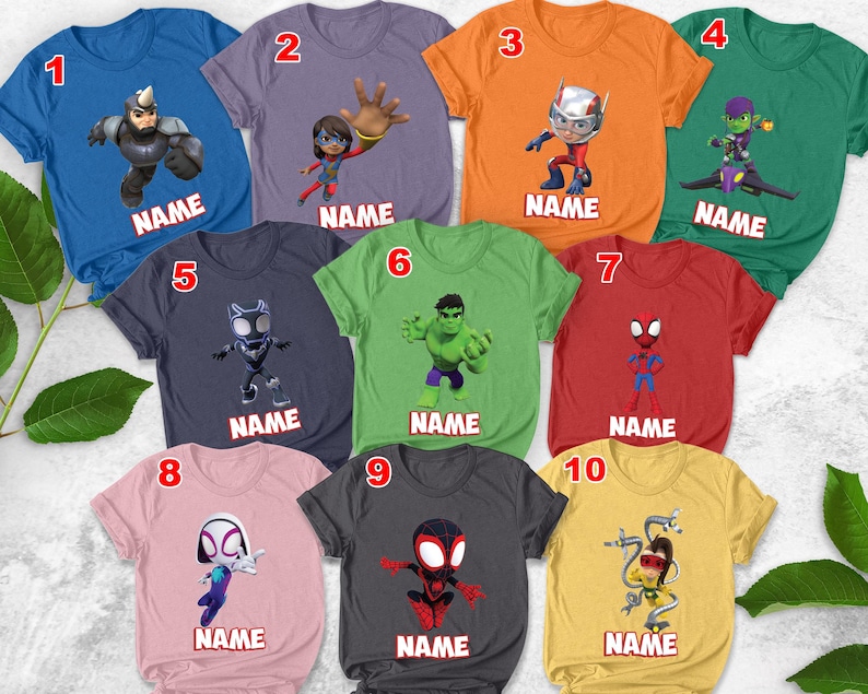 May include: A collection of ten colorful t-shirts featuring various superhero characters. Each shirt has a different design, including characters like Spider-Man and Hulk, with the word "NAME" printed below each character. The shirts are in various colors, including blue, orange, and green.