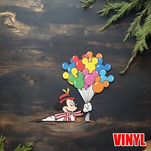 May include: A colorful vinyl sticker featuring Mickey Mouse holding a bouquet of Mickey Mouse-shaped balloons. The balloons are in various colors, including red, yellow, blue, green, pink, and orange. The word "VINYL" is in red letters.