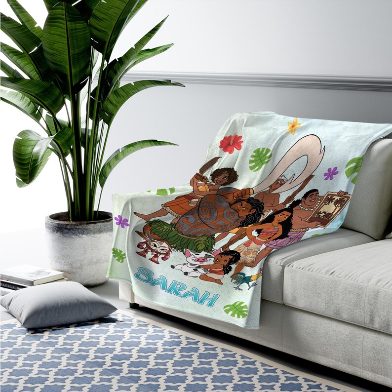 K&ouml;nnte beinhalten: Eine hellblaue Fleecedecke mit einem farbenfrohen Grafikdruck von animierten Charakteren aus dem Film Vaiana, darunter Vaiana, Maui, Pua und Heihei, verziert mit tropischen Blumen und Bl&auml;ttern, mit dem in Blau gedruckten Namen Sarah.