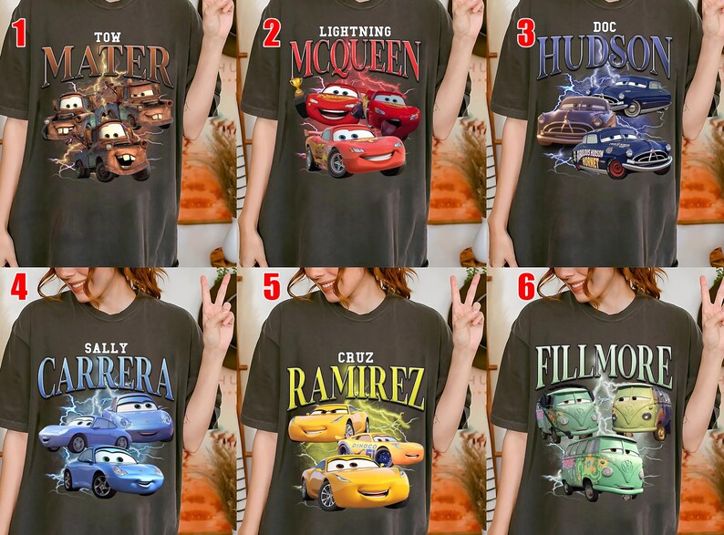May include: Dark grey t-shirts featuring characters from the animated film Cars. Designs include Tow Mater, Lightning McQueen, Doc Hudson, Sally Carrera, Cruz Ramirez, and Fillmore, with lightning bolt graphics.