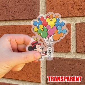 May include: Transparent sticker featuring Mickey Mouse holding a bouquet of Mickey Mouse-shaped balloons in various colors. Mickey is wearing a red and black hat and a red and white striped outfit. The word "TRANSPARENT" is printed in red.