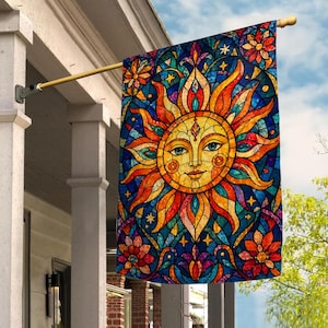 May include: A rectangular garden flag featuring a stained glass style design of a central sun with a human face, surrounded by radiating orange and yellow flames, blue geometric patterns, and floral motifs in red, orange, and purple hues.