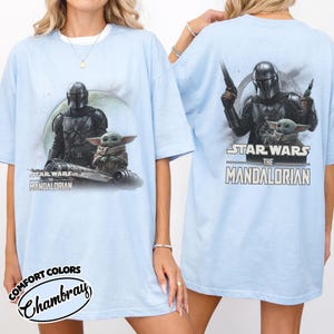 Puede incluir: Camiseta azul claro con un gr&aacute;fico de The Mandalorian y Grogu de Star Wars. La parte delantera muestra a los personajes con una nave, y la parte trasera muestra el texto "Star Wars The Mandalorian".