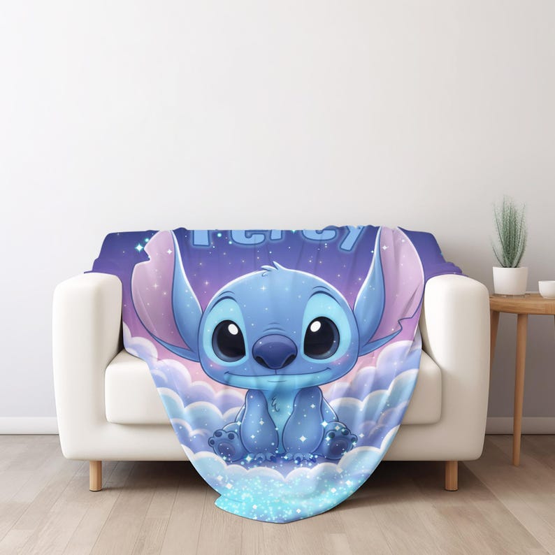 Puede incluir: Una manta suave que presenta un personaje alien&iacute;gena azul con orejas grandes y ojos negros, sentado entre nubes de color p&uacute;rpura claro y azul sobre un fondo de cielo estrellado. La palabra Percy est&aacute; impresa en letras azul claro arriba.