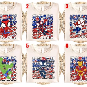 K&ouml;nnte beinhalten: Sechs cremefarbene T-Shirts, jedes mit einem anderen Superhelden in patriotischer Kleidung. Die Designs zeigen Spider-Man, Ghost-Spider, Hulk, Black Panther und Iron Man, mit Text und Grafiken in Rot, Wei&szlig; und Blau.