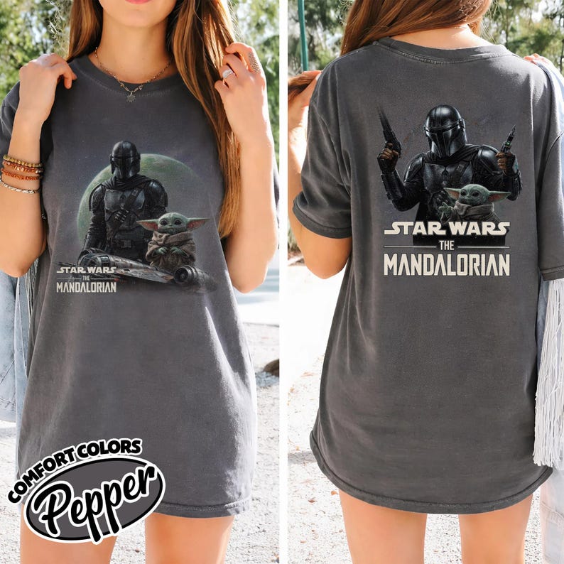 Puede incluir: Camiseta gris oscuro con un gr&aacute;fico de The Mandalorian y Grogu de Star Wars. La parte delantera de la camiseta muestra los personajes con el texto "Star Wars The Mandalorian". La parte trasera de la camiseta tambi&eacute;n tiene los personajes y el texto.