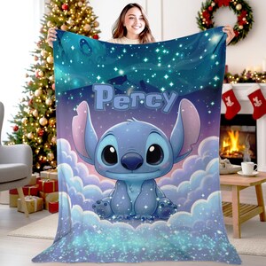 Puede incluir: Una manta de forro polar suave con un personaje alien&iacute;gena azul sentado sobre nubes blancas esponjosas contra un cielo nocturno estrellado azul oscuro. El nombre Percy est&aacute; impreso en letras grandes de color azul claro sobre el personaje.