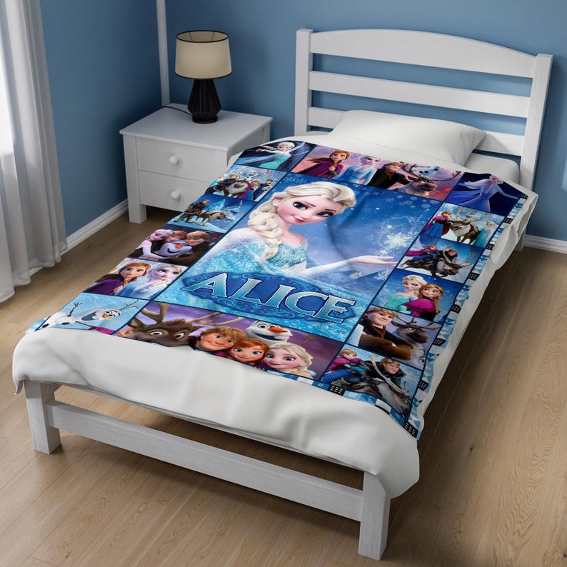 May include: A white bed frame with a mattress covered by a blue and white patterned blanket featuring characters from the movie Frozen. The blanket displays multiple scenes with Elsa, Anna, Olaf, and Sven, and includes the name Alice in blue letters.