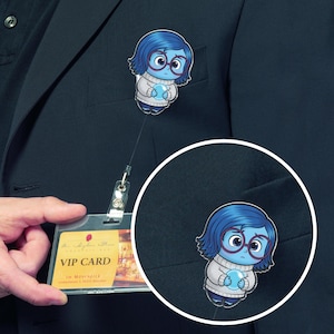 May include: A badge reel featuring a cartoon character with blue hair, glasses, and a white sweater. The character is holding a blue orb. The reel is attached to a VIP card.