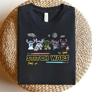 May include: Black t-shirt featuring a graphic of several Stitch characters in various costumes, with the text "Stitch Wars" in yellow and red. The design includes lightsabers and space-themed elements.