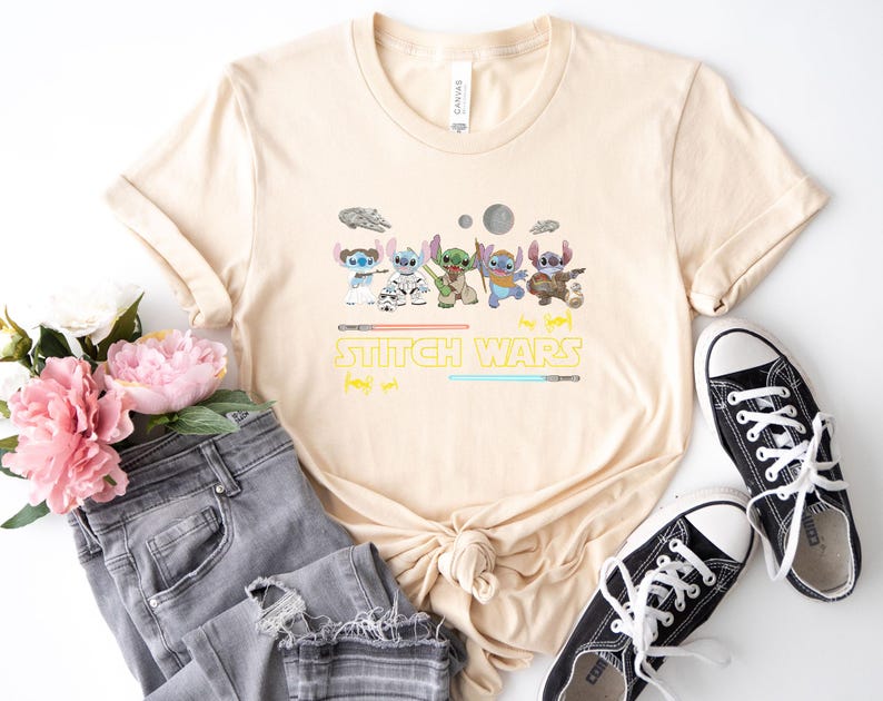 May include: A beige t-shirt featuring a graphic of several cartoon characters with lightsabers and the text "STITCH WARS". The shirt is paired with gray jeans and black canvas sneakers.