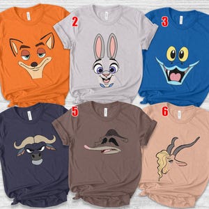 May include: Six short-sleeved t-shirts in various colors, each featuring a cartoon character face. The shirts are orange, gray, blue, navy, brown, and peach. The cartoon faces include a fox, a rabbit, a monster, a bull, a duck, and a gazelle.