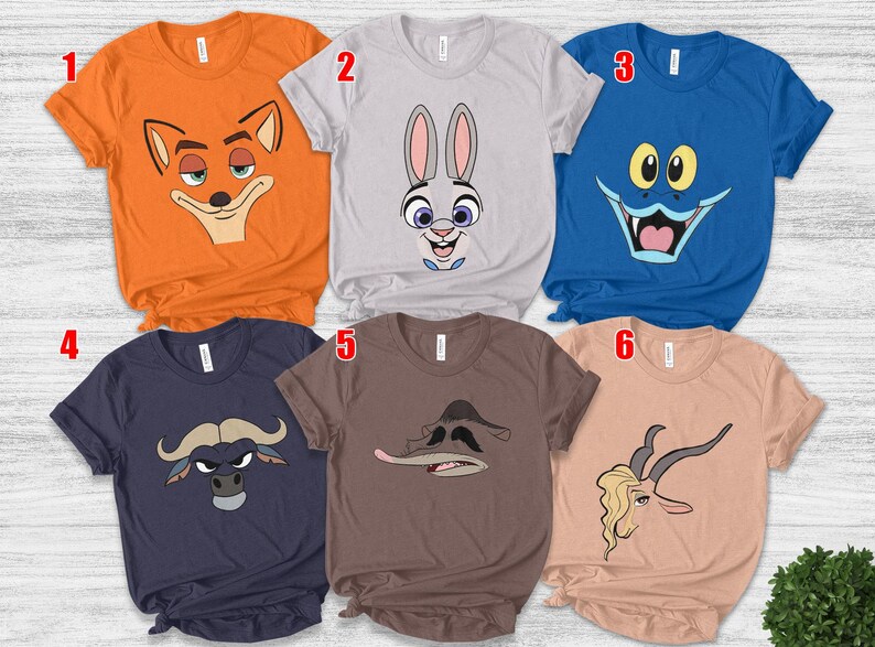 May include: Six short-sleeved t-shirts in various colors, each featuring a cartoon character face. The shirts are orange, gray, blue, navy, brown, and peach. The cartoon faces include a fox, a rabbit, a monster, a bull, a duck, and a gazelle.