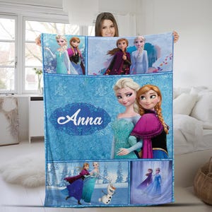 May include: A blue fleece blanket featuring multiple scenes of Elsa, Anna, and Olaf from Frozen. The design includes a large central panel with the name Anna in white script, surrounded by snowflake patterns and various character illustrations.