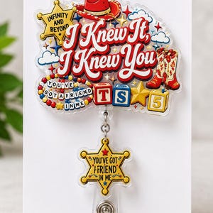Puede incluir: Un portatarjetas de acr&iacute;lico con un dise&ntilde;o colorido que incluye un sombrero de vaquero rojo, botas, bloques de letras y estrellas. El texto dice I Knew It, I Knew You, Infinity And Beyond y You've Got A Friend In Me en un dije de estrella.