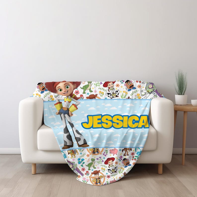 May include: A soft throw blanket featuring a light blue center stripe with the name JESSICA in bold yellow letters. The design includes Toy Story characters like Jessie, Buzz Lightyear, and Rex, surrounded by colorful floral patterns on white.