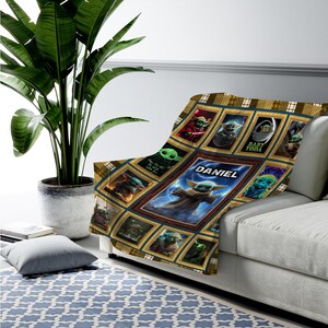 May include: A rectangular throw blanket featuring a grid of framed images of the character Grogu, also known as Baby Yoda, in various poses. The center frame is larger and displays the name DANIEL in white text above a central image of the character.