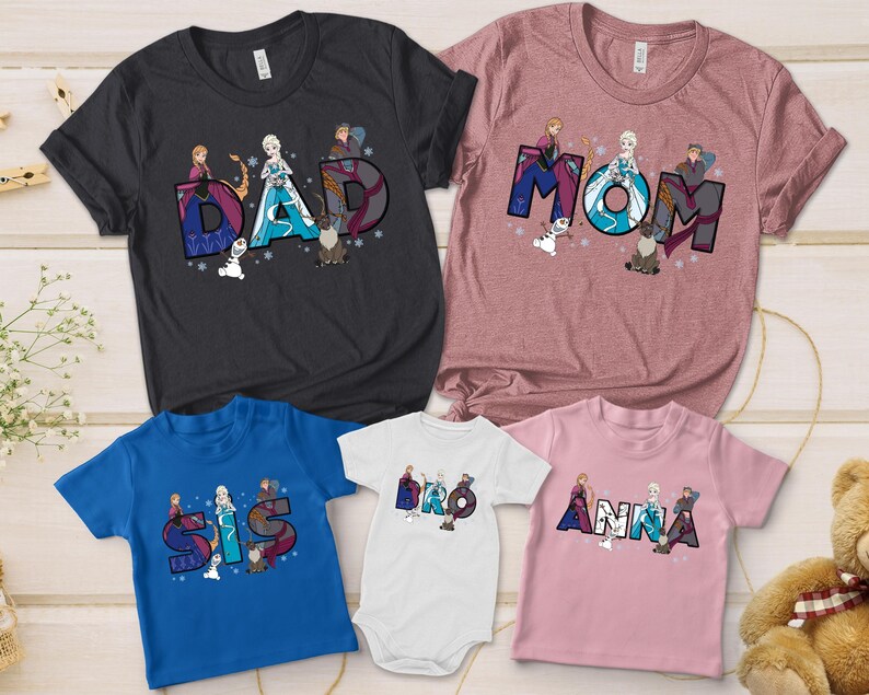 Puede incluir: Una colecci&oacute;n de camisetas y un body con las palabras "DAD", "MOM", "SIS", "BRO" y "ANNA" en una fuente colorida y estilizada. Cada dise&ntilde;o incluye ilustraciones de personajes de una popular pel&iacute;cula de animaci&oacute;n. Las camisetas son de varios colores.
