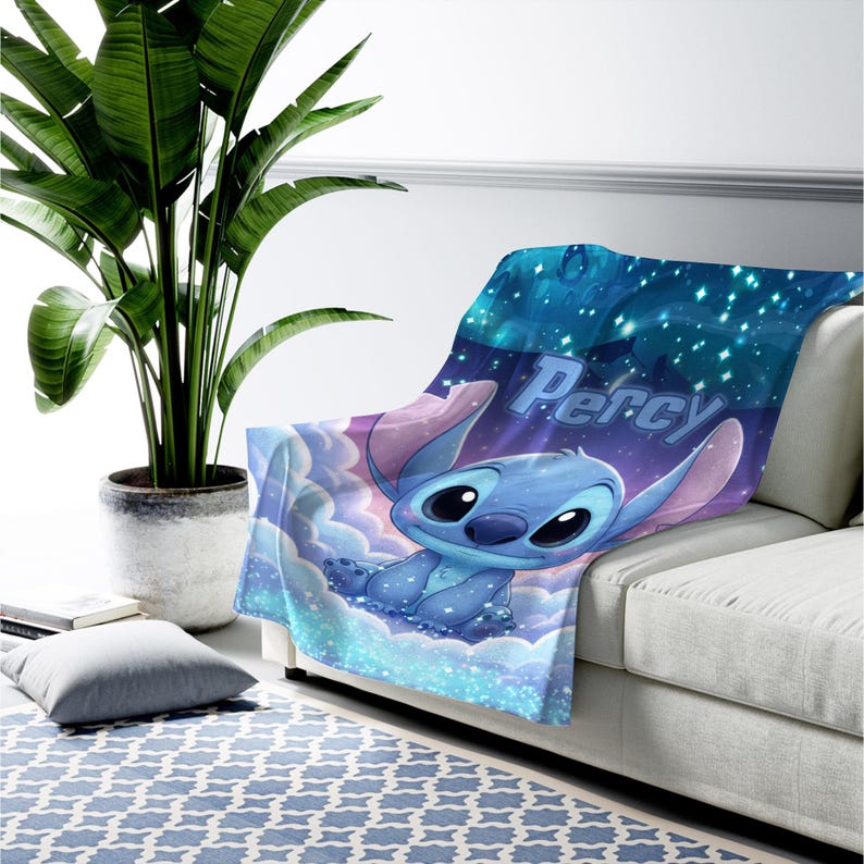 Puede incluir: Una manta suave con un personaje alien&iacute;gena azul sentado sobre nubes azul claro bajo un cielo estrellado azul oscuro. El nombre Percy est&aacute; impreso en una fuente azul claro sobre el personaje, con efectos de luces brillantes.