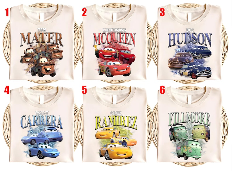 May include: Cream-coloured t-shirts featuring characters from the animated film "Cars." Each shirt displays a different character's name and image: Mater, Lightning McQueen, Doc Hudson, Sally Carrera, Cruz Ramirez, and Fillmore. The designs include illustrations of the cars.