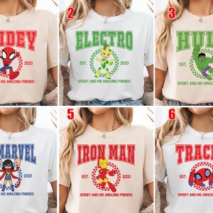 May include: A collection of six t-shirts featuring superhero-themed designs. Each shirt displays a different character's name in bold letters, along with a corresponding graphic and the text "Spidey and His Amazing Friends". The shirts are in various colors.