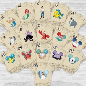 May include: A collection of beige t-shirts featuring various cartoon characters from a popular animated film. Designs include a mermaid, a crab, a fish, and other characters. The shirts are arranged in a circular pattern.
