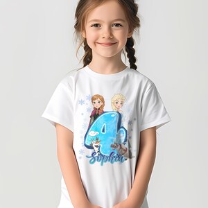 Pode incluir: T-shirt branca com um gr&aacute;fico colorido do n&uacute;mero 4, com as personagens Anna e Elsa do filme Frozen. A t-shirt tamb&eacute;m inclui o nome "Sophia" em uma fonte cursiva.