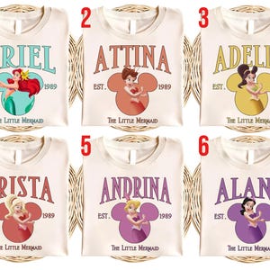 Puede incluir: Seis camisetas color crema con nombres e ilustraciones de personajes de "La Sirenita". Cada camiseta muestra un nombre, el a&ntilde;o 1989 y un dise&ntilde;o en forma de Mickey Mouse con una imagen de personaje.