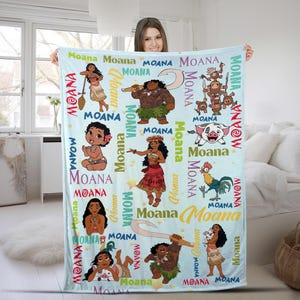 May include: A light blue fleece blanket featuring a repeating pattern of Moana characters including Moana, Maui, Pua the pig, and Heihei the rooster. The design includes the word Moana printed in various colors, fonts, and sizes across the fabric.