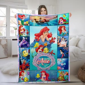 May include: A rectangular fleece blanket featuring a collage of scenes from The Little Mermaid, including Ariel, Flounder, Sebastian, and King Triton. The centre displays a large illustration of Ariel above a decorative frame with the name Anie.