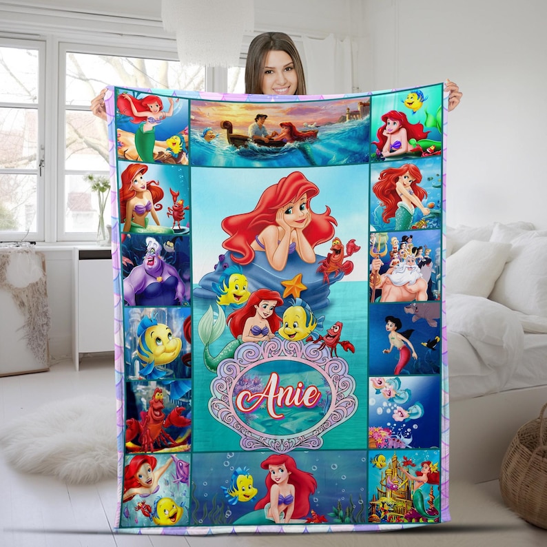 May include: A rectangular fleece blanket featuring a collage of scenes from The Little Mermaid, including Ariel, Flounder, Sebastian, and King Triton. The centre displays a large illustration of Ariel above a decorative frame with the name Anie.