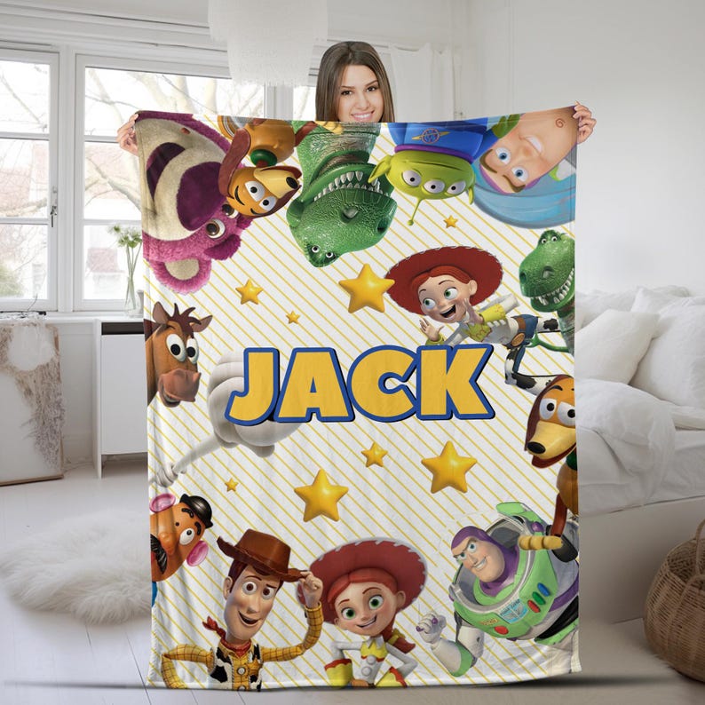 May include: A fleece blanket featuring a yellow and white diagonal striped pattern with various Toy Story characters including Woody, Buzz Lightyear, Jessie, and Rex. The name JACK is printed in large, bold yellow letters with a blue outline.
