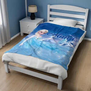 May include: A blue fleece blanket featuring a graphic print of a blonde character in a light blue dress, with the name Anna written in a dark blue script font. The blanket displays a snowy landscape with ice formations and a starry night sky.