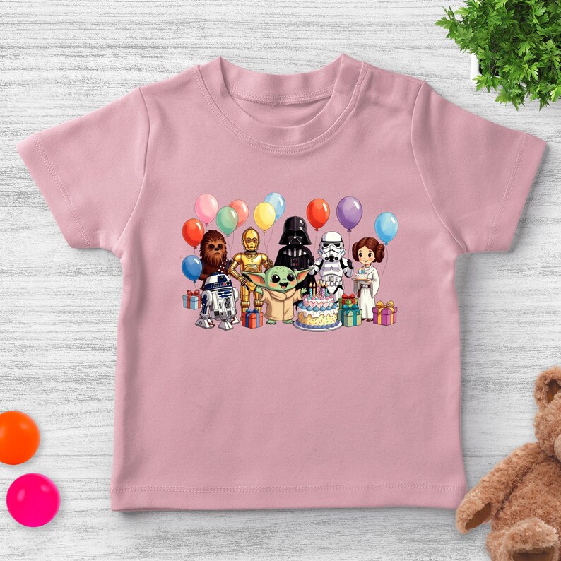 Puede incluir: Camiseta rosa claro con un dise&ntilde;o de personajes de Star Wars, incluyendo Darth Vader, R2-D2 y Baby Yoda, celebrando un cumplea&ntilde;os con globos y una tarta. Un dise&ntilde;o colorido y divertido para ni&ntilde;os.