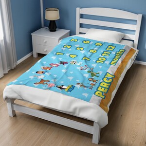 May include: A light blue fleece blanket featuring a repeating white cloud pattern, a yellow numerical sequence from 1 to 12, the word months, and various cartoon character illustrations. The name PERCY is printed in large yellow letters on the side.