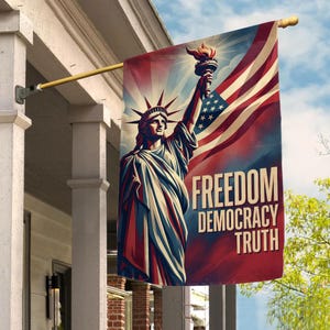 May include: A patriotic flag featuring the Statue of Liberty holding a torch, with the American flag in the background. The flag has the words "FREEDOM DEMOCRACY TRUTH" in white text. The flag is hanging on a porch.