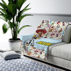 May include: A soft throw blanket featuring a repeating pattern of Toy Story characters including Woody, Buzz Lightyear, Jessie, and Mr. Potato Head. The blanket has a light blue section with the name JESSICA printed in bold yellow letters.