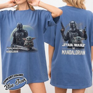 Puede incluir: Camiseta azul con un gr&aacute;fico de The Mandalorian y Grogu de Star Wars. El dise&ntilde;o frontal muestra a los personajes con el texto "Star Wars The Mandalorian". La parte posterior de la camiseta tambi&eacute;n tiene el mismo gr&aacute;fico. La camiseta es de la marca Comfort Colors.