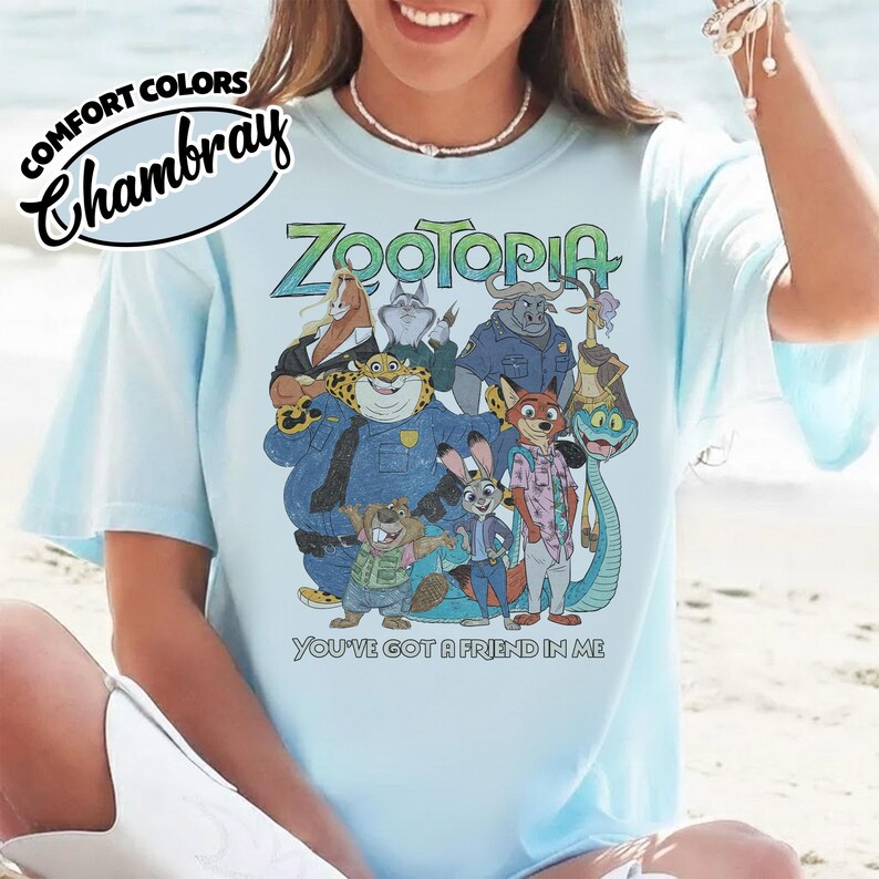 May include: Light blue t-shirt featuring a colorful graphic of characters from the animated movie "Zootopia." The shirt includes the text "Zootopia" in green and blue, and the phrase "You've got a friend in me."