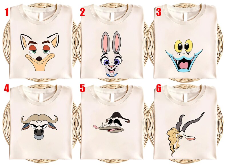May include: Six cream-colored t-shirts, each featuring a different cartoon character face. The designs include a fox, a rabbit, a dragon, a buffalo, a duck, and a gazelle. The shirts are displayed on a woven surface.