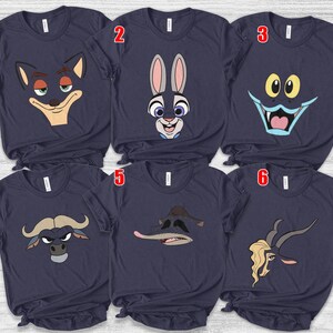 May include: Navy blue t-shirts featuring cartoon character faces. The designs include a fox, a rabbit, a monster, a bull, a duck, and a goat. Each shirt has a crew neck and short sleeves.
