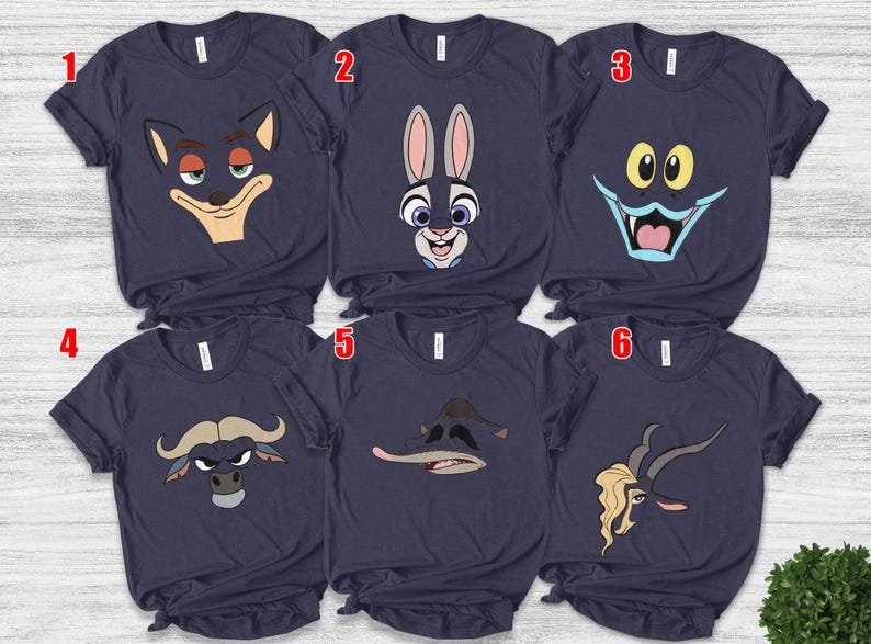 May include: Navy blue t-shirts featuring cartoon character faces. The designs include a fox, a rabbit, a monster, a bull, a duck, and a goat. Each shirt has a crew neck and short sleeves.